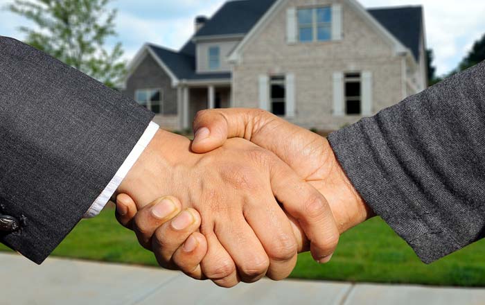Two men in suits shaking hands in front a property