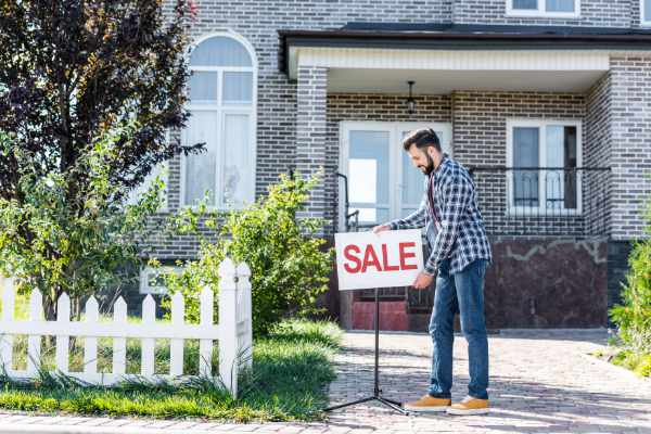 Photo of a man putting a Sale sign in front of his house