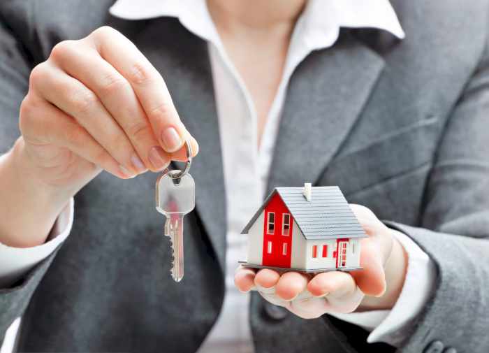 Photo of a real estate agent holding house keys and a small house