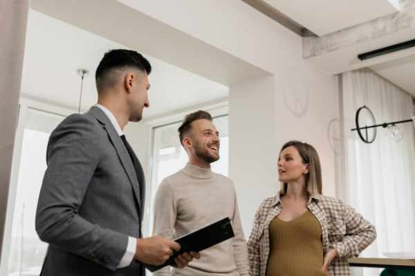 Photo of a real estate agent showing a property to a young couple