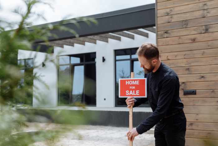 Photo of an agent putting a home for sale sign in front of a house
