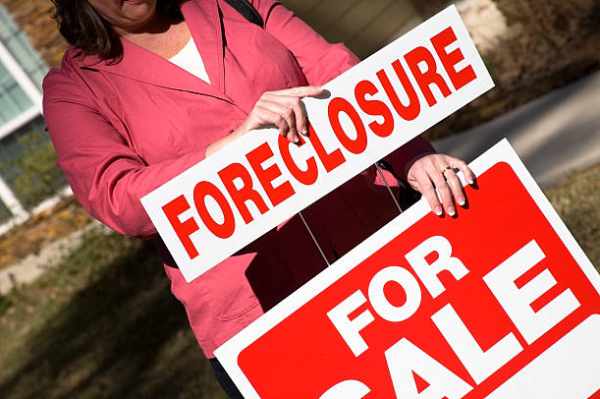 Photo of a woman putting a Foreclosure rider on a For Sale sign