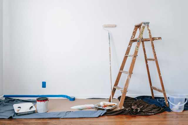 Photo of a room about to be painted with a ladder, rollers, drop clothes, paint cans, brushes