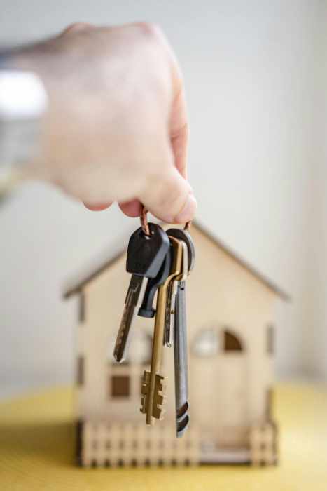 Photo of a hand hold house keys in front of a small model home