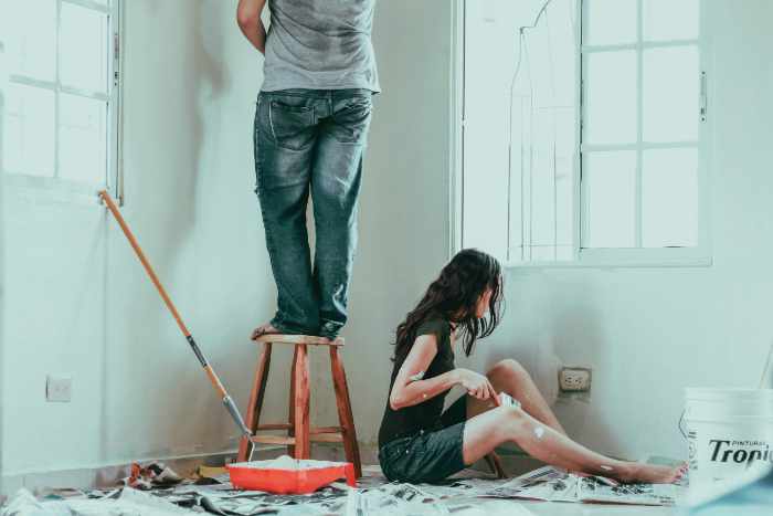 Photo of a man paiting the ceiling while standing on a stool and a woman sitting painting the way - The Seasonal Home Maintenance Checklist Every Homeowner Needs