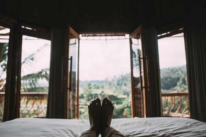 Photo of a person laying in bed looking out the windows of his vacation home - Giving Your Vacation Home a New Look: 9 Things To Do