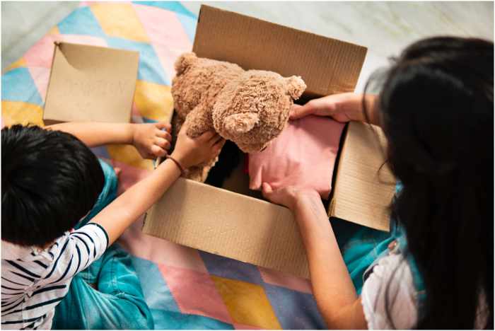 Photo of a family unpacking a box with a toy stuffed bear in it - 4 Ways to Prepare Your Kids For a Move: A Guide For Families