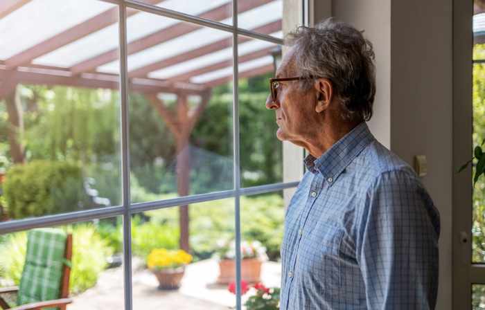 Photo of a man looking out a window onto his backyard patio - Identifying the 5 Hidden Sources of Noise Pollution in Your Home