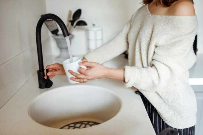 Photo of a woman filling a glass with water - Hard Water in Louisville Homes: What Buyers and Homeowners Should Know