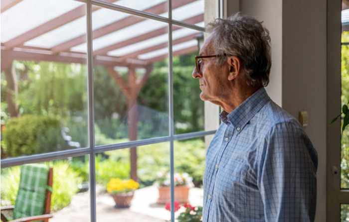 Photo of a senior man looking out the window onto his patio - 5 Key Downsizing Tips for Seniors